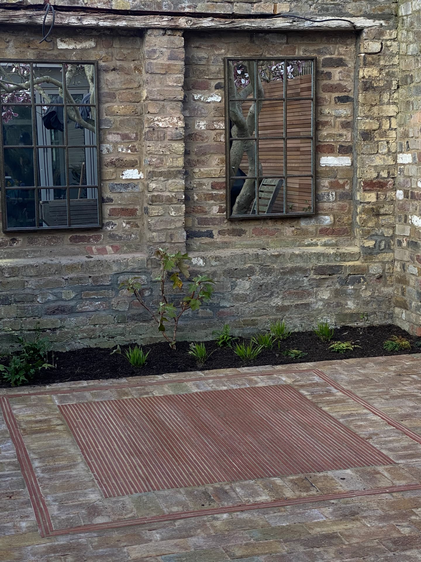 Reclaimed brick terrace with a woven red brick panel against an old stock brick wall