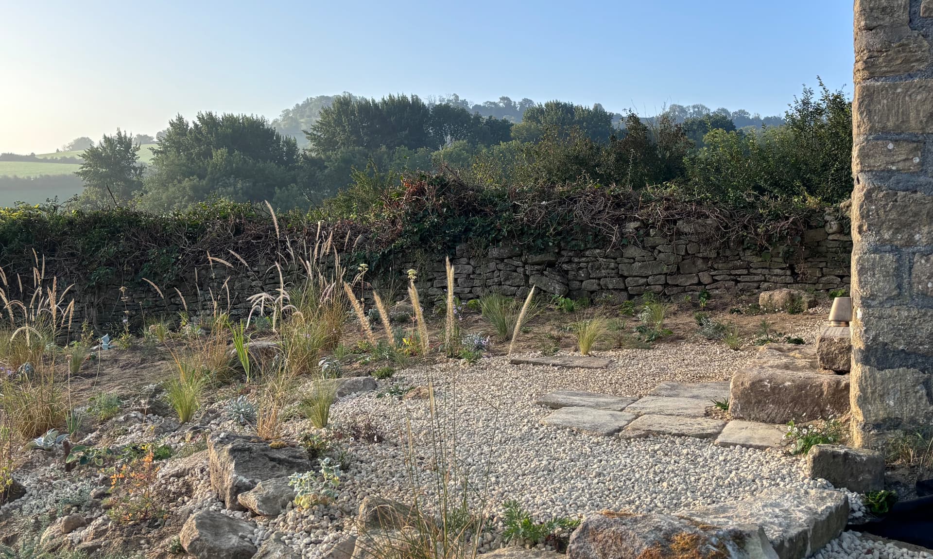 Gravel and stone garden with ornamental grasses in front of a drystone wall, hills beyond, landscape design by GHS Spaces, landscape designer in Bristol