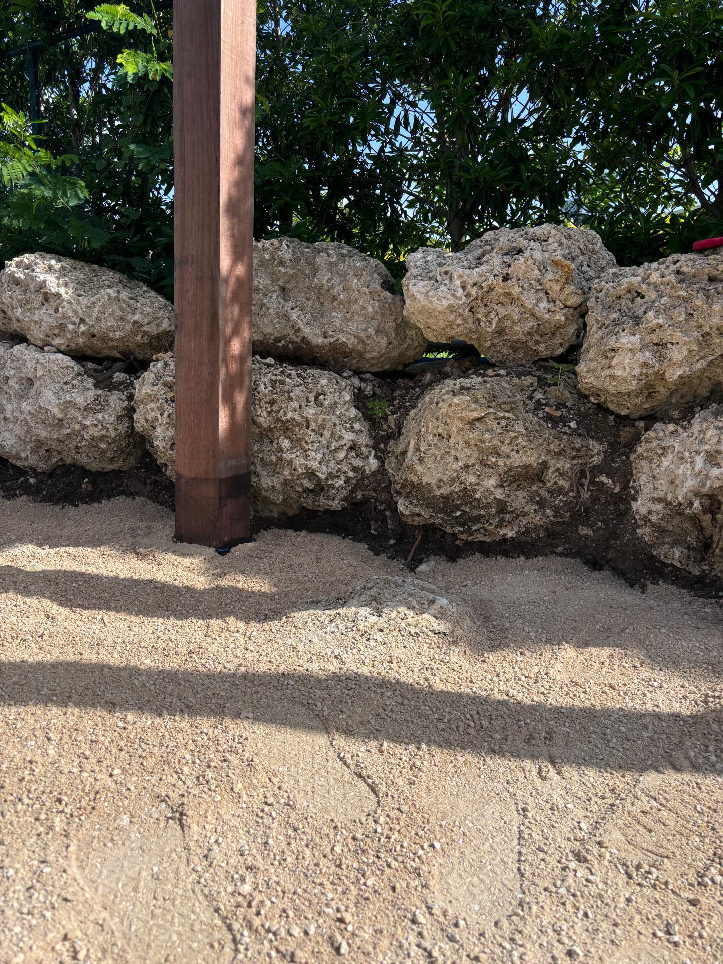 Coral stone retaining wall with hardwood post set into gravel paving